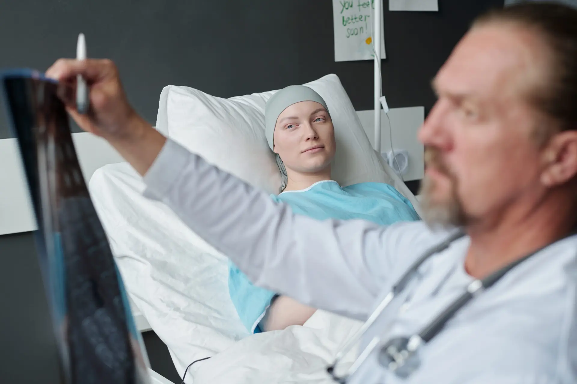 Young woman with brain cancer lying in bed and looking at doctor